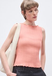 Ροζ ριμπάτη αμάνικη μπλούζα με κυματιστή λαιμόκοψη και τελείωμα, κατασκευασμένη από υφή ύφασμα. Το μοντέλο κρατάει ένα λευκό τσαντάκι και φορά σκούρο παντελόνι.