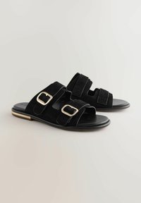 Schwarze Wildleder-Sandalen mit zwei verstellbaren Riemen, goldenen Schnallen und einer flachen Sohle. Sie verfügen über ein glattes Lederfußbett und kontrastierende Verzierungen.