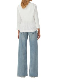 Witte geribde katoenen lange mouw top, gecombineerd met lichtblauwe wijdvallende denim jeans. De jeans hebben een vervaagde textuur en subtiele achterzakken.