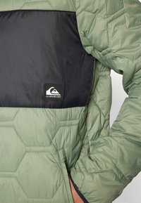 Kurtka puchowa Quiksilver z heksagonalnym pikowaniem w kolorze zielonym, górną częścią w jednolitym czarnym kolorze oraz naszywką z logo z przodu.