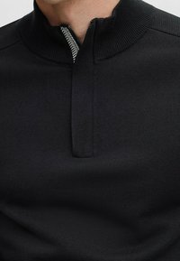 Black pullover with a half-zip collar, featuring ribbed detailing at the collar and a textured fabric. Simple, minimalist design.