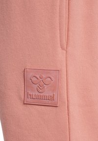 Jasnoróżowy sweatshirt z teksturowaną, gumowaną naszywką z logo z napisem "hummel" oraz symetrycznym wzorem powyżej. Miękka faktura materiału.