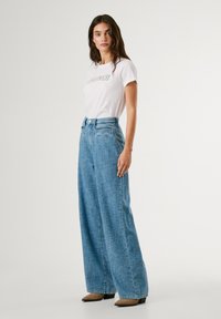 Wide-leg blue denim jeans with a textured finish and front pockets, paired with a plain white t-shirt featuring a graphic print.