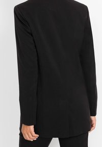 Czarna dopasowana marynarka o prostym kroju, z długimi rękawami i delikatną fakturą. Posiada pojedynczy rozcięcie z tyłu oraz minimalistyczne detale metalowe.