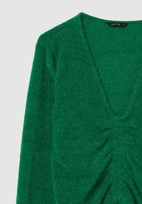 Maglione verde con trama a coste, scollo a V profondo e dettaglio arricciato in vita. Realizzato in materiale morbido e peloso; etichetta visibile all'interno del collo.