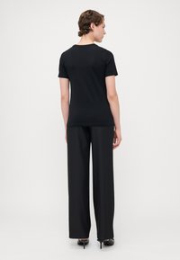 Svart t-skjorte med korte ermer, tettsittende fasong, parret med svarte vidde bukser, glatt tekstur og enkel design.