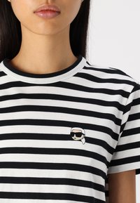 Camiseta de rayas en blanco y negro con cuello redondo y mangas cortas, que presenta un pequeño diseño bordado en el pecho.