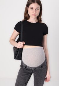 Camiseta negra corta, banda elástica gris en la cintura, combinada con jeans de mezclilla gris oscuro con cierre de botón, sostenida con un bolso negro de hombro.