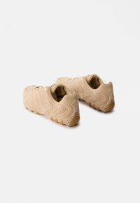 Bežid sueded spordijalanõud tekstureeritud lainekujundusega, paeltega kinnitamine ja kummist välistald. Omab külje peal logo ja kontrastsete suuri aktsentidega.