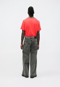 T-shirt vermelha de mangas curtas combinada com jeans pretos de perna larga; apresenta passadores para cinto e bolsos traseiros; tecido liso com um ajuste descontraído.