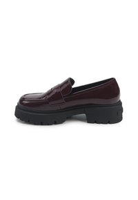 Burgundia läikivast nahast loafers, millel on massiivne must kummist alus ja paks konts, külgvaates valge tausta peal.