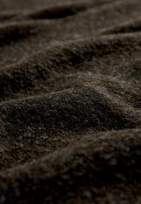 Hnědá vlněná tkanina s texturovaným povrchem a viditelnými vlákny, vykazující variace v odstínech a měkkou, hmatovou kvalitu.