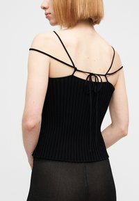 Μαύρο τοπ με ριμπ ύφανση και λεπτές ρυθμιζόμενες τιράντες, με λεπτομέρεια δεσίματος στην πλάτη. Το υλικό έχει υφή και εφαρμοστή γραμμή.
