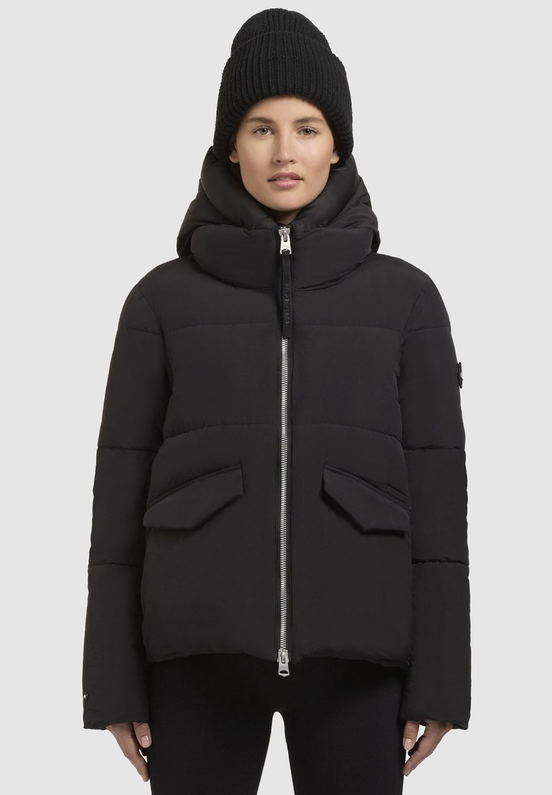 Schwarze Pufferjacke mit hohem Kragen, Vorderreißverschluss und zwei Fronttaschen. Strukturiertes Material mit einer gesteppten Optik zur Isolierung.