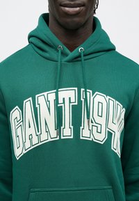 Sudadera con capucha verde con la inscripción "GANT 1944" en blanco en el pecho, con bolsillo frontal y cordones ajustables en la capucha.