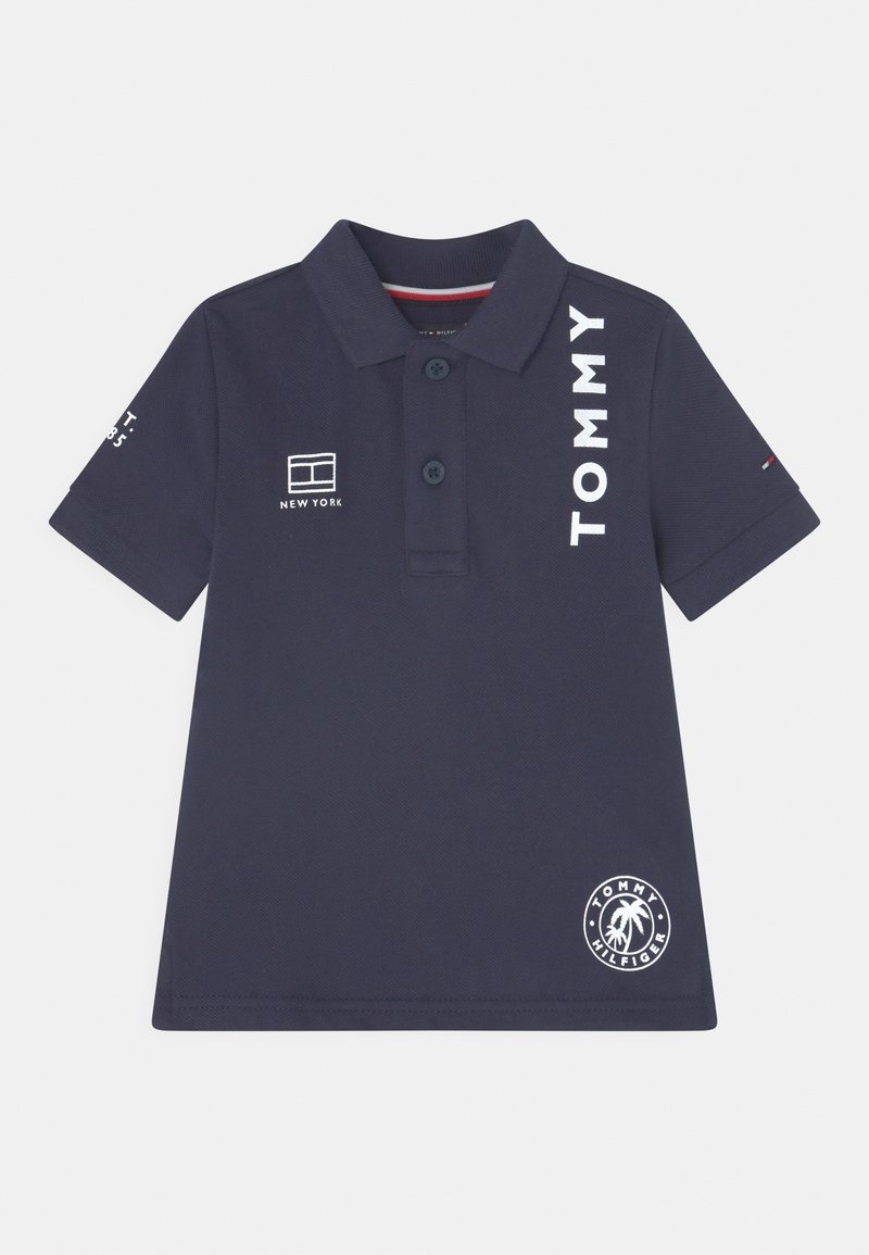 Polo bleu marine à manches courtes avec col, deux boutons, texte "TOMMY", logo New York et emblème de palmier Tommy Hilfiger.