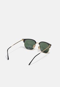 Black and gold sunglasses with green tinted lenses, angular shape, metal frame, and curved black temple arms for secure fit.