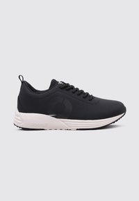 Zapatillas deportivas negras con un upper liso, cierre de cordones y entresuela blanca. Presenta un logotipo destacado y una suela texturizada para un mejor agarre.