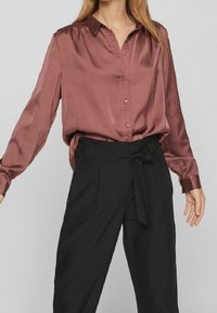 Bordeaux satinskjorta med knappar och långa ärmar, en krage, samt svarta högmidjade byxor med knytbälte och vida ben.