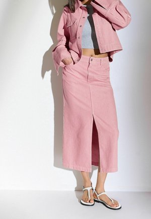 Striped pink denim jacket and matching skirt with a front slit, paired with white sandals. Material is textured; design is fitted.