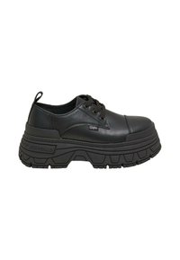 Zapatos de cuero negro con cordones y suela de goma negra gruesa. Presentan una puntera elevada y un sutil branding en el costado.