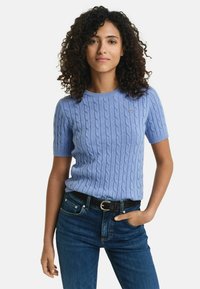 Pull bleu à manches courtes avec un design en tricot torsadé texturé. Doté d'un col rond et d'un petit logo. Assorti à un jean bleu foncé et à une ceinture noire.