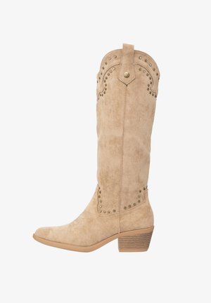 Bottes montantes en daim beige avec des clous décoratifs, un bout arrondi et un talon empilé. Le design présente un bord supérieur festonné.