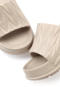 Beige Plattform-Sandalen aus einem strukturierten synthetischen Material, mit einer Aussparung im Zehenbereich und gestickten Zickzackmustern an den Riemen.