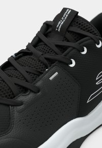 Chaussure de sport noire avec un corps en cuir texturé, une tige en mesh pour la respirabilité, des lacets plats et une semelle en caoutchouc blanche. Présente une marque minimale.