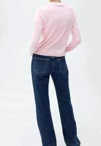 Hellrosa Pullover mit geripptem Saum, kombiniert mit dunkelblauen weiten Jeans mit Gesäßtaschen. Glatte Textur und entspannter Schnitt.