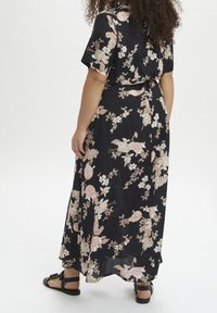 Blomster maxi kjole i mørkeblå med lyserøde og cremefarvede blomster. Korte ærmer, indsnævret talje og let stof. Sorte sandaler synlige.