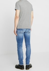 Camiseta de manga corta gris combinada con jeans ajustados de color azul claro y botas negras hasta el tobillo. La tela parece suave y los jeans tienen un acabado desgastado.