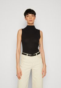 Must mustripsiga ilma varrukateta turtleneck-top, mis on paaritatud kreemjas laia säärega pükstega ja musta vöödiga. Lihtne disain tekstureeritud kangaga.