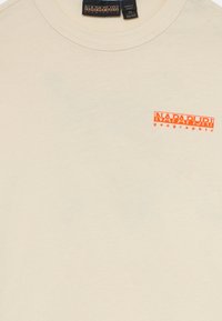 Beige tričko s krátkým rukávem a kulatým výstřihem se malým oranžovým logem "Napapijri geographic" na levé straně hrudi a textilní etiketou na límci.