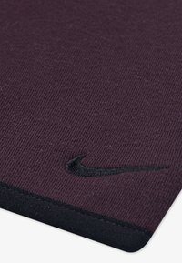 Fialový textil s pruhovanou textúrou, na jednej strane s čiernym vyšitým logom Nike swoosh a čiernym okrajom pozdĺž spodného okraja.