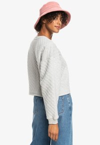 Gray quilted cropped sweatshirt with ribbed cuffs, paired with high-waisted blue jeans and a pink corduroy bucket hat.