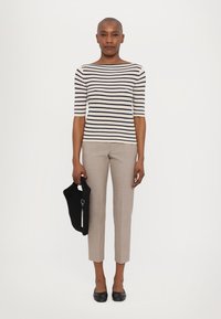 Pull ajusté à rayures en crème et marine, associé à un pantalon tailleur beige clair. Le mannequin tient un sac en tricot noir. Chaussures plates noires.