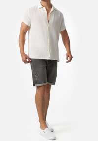 Kurzärmliges, strukturiertes weißes Hemd mit Kragen, kombiniert mit grauen Shorts mit umgeschlagenen Säumen und seitlichen Details sowie weißen Slippern.