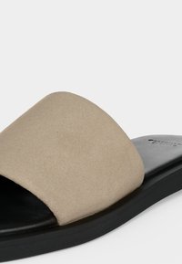 Sandale mule beige en daim avec une large bride et une semelle noire, conçue pour un usage décontracté.