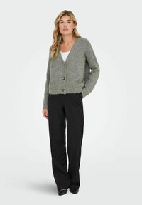 Cárdigan de punto gris con escote en V, tres botones, dobladillo acanalado y mangas largas, combinado con pantalones de pierna ancha negros.