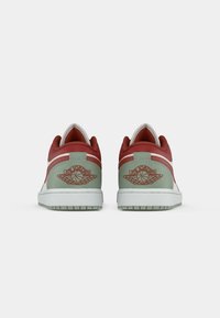 Une paire de baskets basses avec des accents verts et rouges, vues de l'arrière, arbore le logo ailé de basketball Air Jordan sur les talons.
