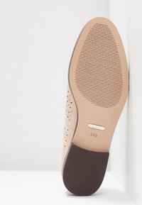 Semelle de chaussure beige avec grip texturé au niveau des orteils et du talon, taille marquée 6,5B, présentée sur fond blanc et coin de mur.