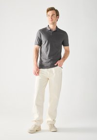 Dark gray short-sleeve polo shirt, fitted design, paired with loose-fitting white trousers and light beige sneakers. Simple, clean lines.