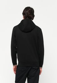 Felpa nera con finitura testurizzata, cappuccio con cordino e polsini a coste con accenti a righe. Design semplice senza grafiche visibili.