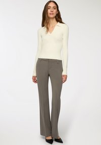Skręcony sweter z długim rękawem w kremowym kolorze z dekoltem w serek, połączony z szarymi, dopasowanymi spodniami. Całość uzupełniają czarne szpilki z ostro zakończonym noskiem.