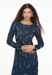 Navyblaues Kleid mit langen Ärmeln, verziert mit silbernen Blattmustern und Pailletten, mit Rundhalsausschnitt und taillierter Passform.