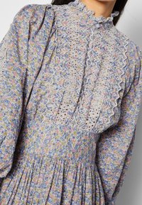 Květnaté šaty s modrými, růžovými a žlutými květy, s krajkovými panely, knoflíky po průramku, vysokým volánkovým límcem a se sešitým pasem.
