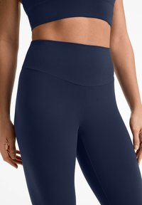 Leggings taille haute bleu marine fabriqués en tissu lisse et extensible, avec un design sans coutures et une large taille pour le confort et le soutien.