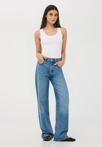 Jeans in denim blu a gamba larga con vita alta, cinque tasche e cuciture a vista. Abbinati a un top bianco aderente.
