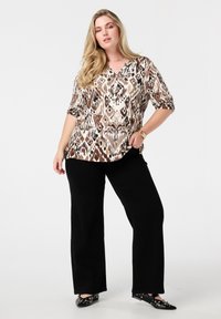 Bruin en beige geblokt top met een V-hals en opgerolde mouwen, gecombineerd met zwarte wijde broek en zwarte flats met versieringen.